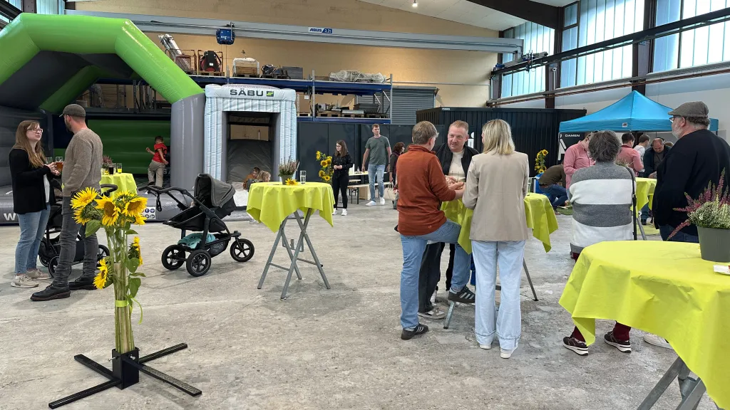 Gäste und Familien im Gespräch an Stehtischen beim Indoor-Familienfest in der Halle bei SÄBU.