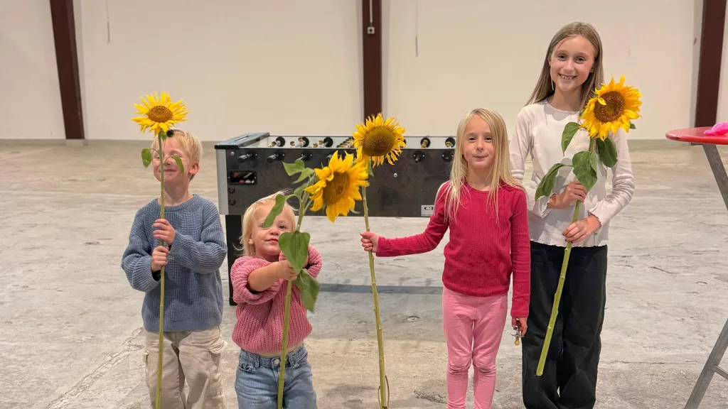 Vier fröhliche Kinder halten Sonnenblumen beim Familienfest zum Weltkindertag vor einem Tischkicker.