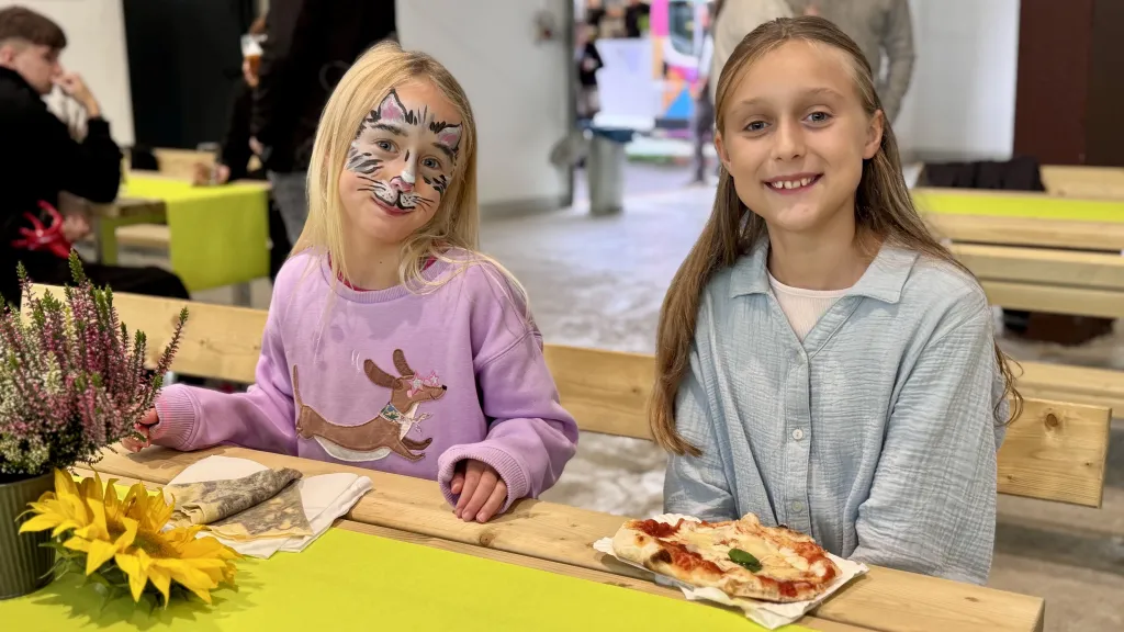 Zwei Mädchen mit Kinderschminken genießen Pinsa und Crêpes am Bierzelt-Tisch beim SÄBU-Familienfest.